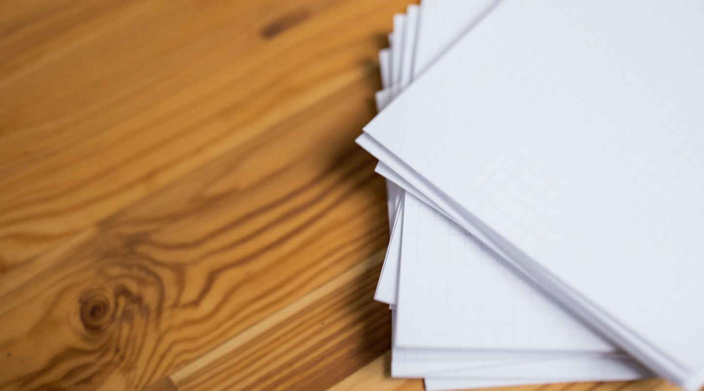A neat stack of plain blank grid-ruled paper sheets, corners aligned, with a plain ruler beside them.